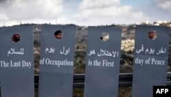 Des militants israéliens et palestiniens brandissent des pancartes en forme de barrière lors d’une marche pour la paix pour protester contre le projet controversé de mur séparant la ville cisjordanienne de Beit Jala et Jérusalem, le 15 janvier 2016.