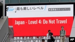 Para pejalan kaki mengenakan masker, berjalan di depan layar di Tokyo, yang menunjukkan berita tentang peringatan AS terhadap kunjungan ke Jepang, Selasa, 25 Mei 2021.
