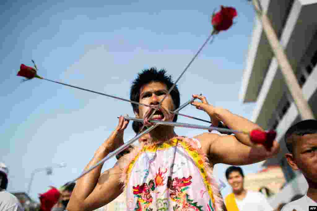 A devotee of the Loem Hu Thai Su shrine has a metal rods with roses pierced through his cheeks as he parades during the annual Vegetarian Festival in Phuket, Thailand.