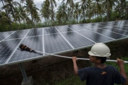 Seorang karyawan PT Perusahaan Listrik Negara (PLN) membersihkan permukaan panel surya di pembangkit listrik tenaga surya di Pulau Gili Meno, pada 9 Desember 2014. (Foto: Antara/Widodo S. Jusuf via Reuters)