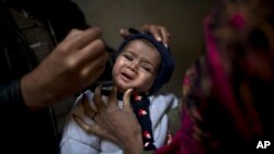 A Pakistani health worker, right, gives a polio vaccine to a child held by her mother at their home in Rawalpindi, Jan. 20, 2014.