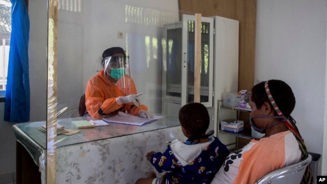 Seorang tenaga kesehatan berbicara dengan seorang perempuan dibalik pelindung plastik untuk mencegah penularan virus corona di sebuah puskesmas di Yalimo, Provinsi Papua, 21 April 2020. (Foto: AP)