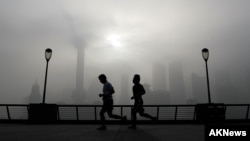 People jog past the Pudong Financial District shrouded with fog and pollution at the Shanghai Bund in Shanghai, China, Thursday, April 14, 2016. 