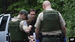 Washington State Fish & Wildlife Police confer with someone from the King County Medical Examiner’s Office and a King County Sheriff’s Office deputy outside Snoqualmie, Wash., following a fatal cougar attack, May 19, 2018. 