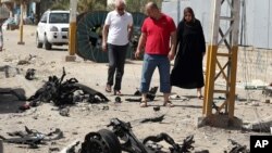 Civilians pass by the site of a car bomb attack in Baghdad's northern neighborhood of Shaab, Iraq, June 25, 2015. 