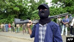 FILE - A masked Abu Sayyaf gunman and other rebels gather outside a mosque in Bandang in Jolo island, Philippines, May 27, 2000.