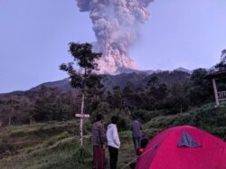 Beberapa wisatawan memperhatikan Gunung Merapi yang sedang erupsi, di Cangkringan, Sleman, Yogyakarta, 3 Maret 2020. (Foto: Antara via Reuters)