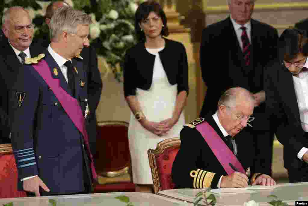 King Albert II (2nd R) of Belgium, watched by his son Crown Prince Philippe (L) and Prime Minister Elio Di Rupo (R), signs an act of abdication during a ceremony at the Royal Palace in Brussels, July 21, 2013.&nbsp;