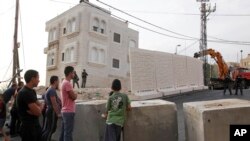 Palestinians watch a wall being built between Palestinian and Jewish neighborhoods in Jerusalem Sunday, Oct. 18, 2015. 