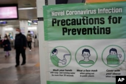People wearing face masks pass by a poster of precautions against coronavirus at a subway station in Seoul, South Korea, Jan. 25, 2022.