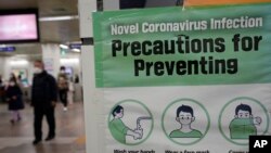 People wearing face masks pass by a poster of precautions against coronavirus at a subway station in Seoul, South Korea, Jan. 25, 2022. 