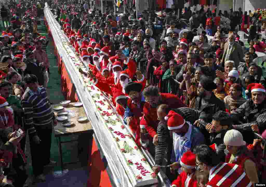 A man wearing a Santa hat (R) prepares to cut a cake that is 201-feet (61 meters) long as boys dressed in Santa Claus costumes cheer during Christmas celebrations in the northern Indian city of Chandigarh. 