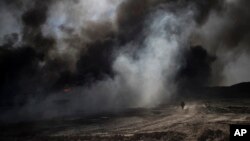 An oil worker walks next to burning oil fields in Qayara, south of Mosul, Iraq, Tuesday, Nov. 22, 2016. 