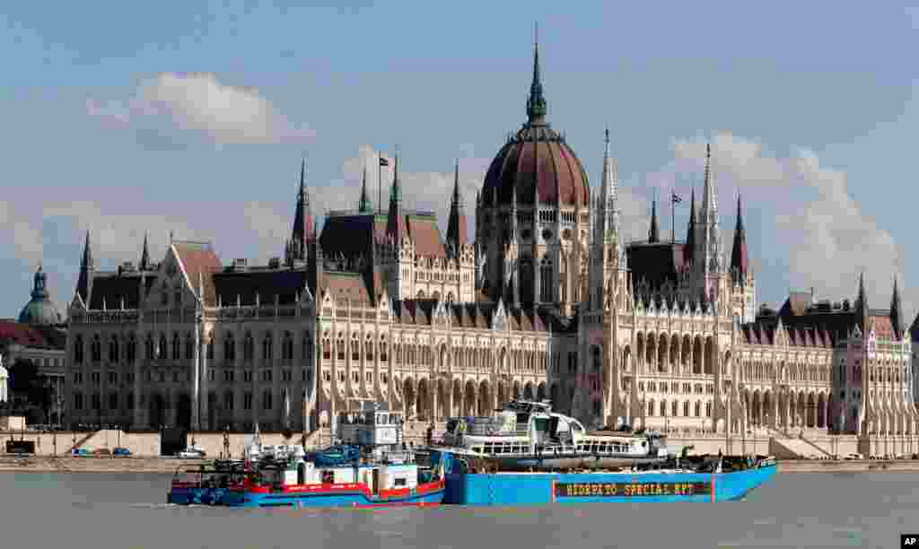 A barge carries the sightseeing boat, right, past the house of parliament on the Danube river after it was lifted from riverbed in Budapest, Hungary.