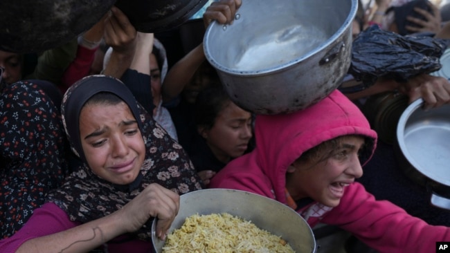 Palestinian girls struggle to reach for food at a distribution center in Khan Younis, Gaza Strip, Dec. 6, 2024.