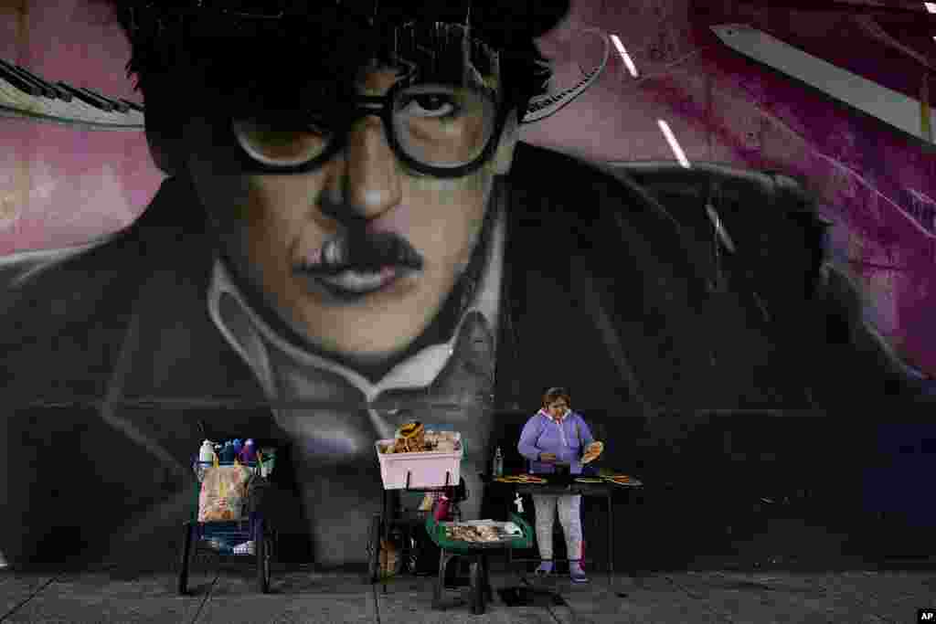 A person sells bread under a bridge decorated with a mural of musician Charly Garcia in Buenos Aires, Argentina.