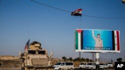 FILE - U.S. military convoy drives through the town of Qamishli, Syria, by a poster showing Syrian President Bashar al-Assad on Oct. 26. 2019. 