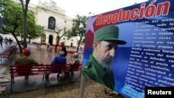 FILE - People sit in front of a billboard with a message about Cuba's late President Fidel Castro in Santa Clara, Cuba, Nov. 30, 2016.