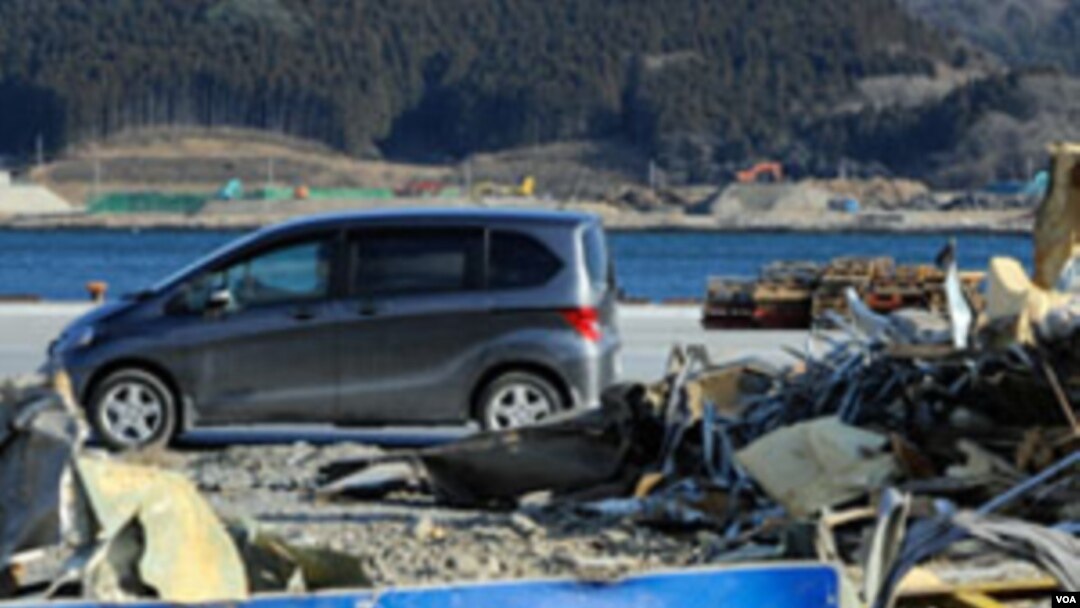 Sebuah mobil lewat di depan tumpukan puing-puing (15/1) akibat bencana tsunami di dermaga di Ofunato, Iwate, hampir satu tahun setelah tsunami menghancurkan daerah tersebut pada 11 Maret 2011 (AFP).