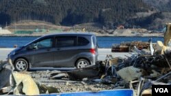 Sebuah mobil lewat di depan tumpukan puing-puing (15/1) akibat bencana tsunami di dermaga di Ofunato, Iwate, hampir satu tahun setelah tsunami menghancurkan daerah tersebut pada 11 Maret 2011 (AFP).