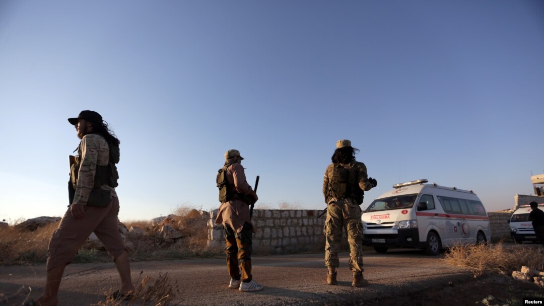 FILE - An ambulance passes by Islamist rebels from Hayat Tahrir al-Sham outside the villages of al-Foua and Kefraya,Syria July 18, 2018. 