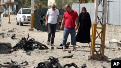 Warga melewati lokasi serangan bom mobil di Shaab, Baghdad, Irak (25/6). (AP/Hadi Mizban)