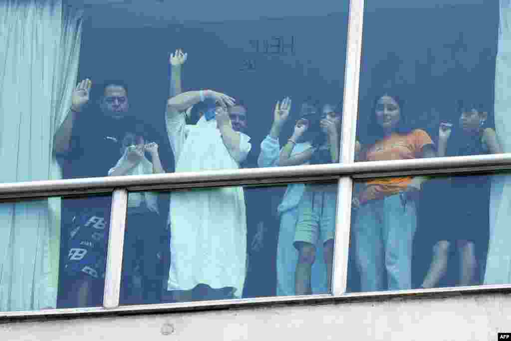 Migrants deported from the U.S. gesture as they look out the window of the Decapolis Hotel where they are temporarily staying in Panama City, Feb. 18, 2024.&nbsp;Panama&#39;s government denied&nbsp; that migrants deported by the United States who were seen holding up signs to hotel windows pleading for help were being held against their will.