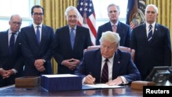 U.S. President Donald Trump signs the $2.2 trillion coronavirus aid package bill as Treasury Secretary Steven Mnuchin, Senate Majority Leader Mitch McConnell (R-KY), House Minority Leader Kevin McCarthy (R-CA) and Vice President Mike Pence stand by during a signing ceremony in th