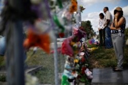 FILE - People mourn in front of flowers placed in the fence of the Marjory Stoneman Douglas High School following a mass shooting in Parkland, Florida, Feb. 18, 2018.