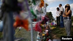 FILE - People mourn in front of flowers placed in the fence of the Marjory Stoneman Douglas High School following a mass shooting in Parkland, Florida, Feb. 18, 2018. 