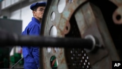 A North Korean worker looks from behind a piece of machinery at the Pyongyang 326 Electric Wire Factory, seen during a press tour on Friday, May 6, 2016.