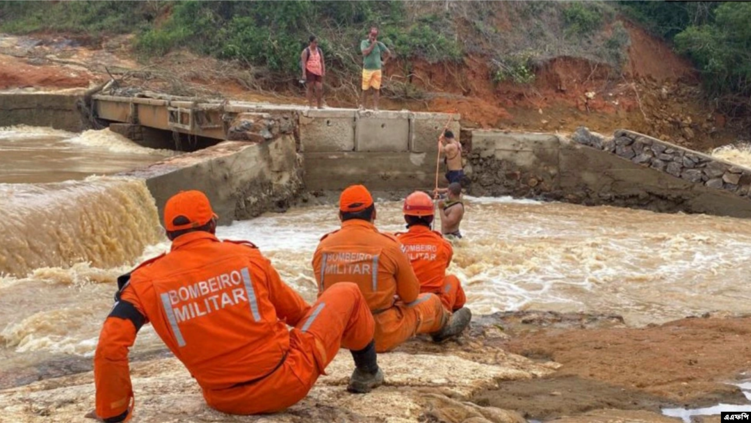 Para petugas pemadam kebakaran membantu warga menyebrangi sungai setelah salah satu jembatan di wilayah Itamaraju, di selatan Bahia, Brasil, rusak akibat hujan deras yang melanda pada 12 Desember 2021. (Foto: AFP/Bahia State Fire Department)