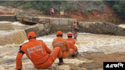 Para petugas pemadam kebakaran membantu warga menyebrangi sungai setelah salah satu jembatan di wilayah Itamaraju, di selatan Bahia, Brasil, rusak akibat hujan deras yang melanda pada 12 Desember 2021. (Foto: AFP/Bahia State Fire Department)