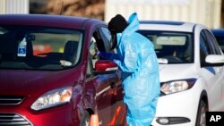 A medical technician performs a nasal swab test on a motorist at a COVID-19 testing site near All City Stadium, Dec. 30, 2021, in Denver. With the rapid spread of the omicron variant, test sites have strained to meet demand across the nation.