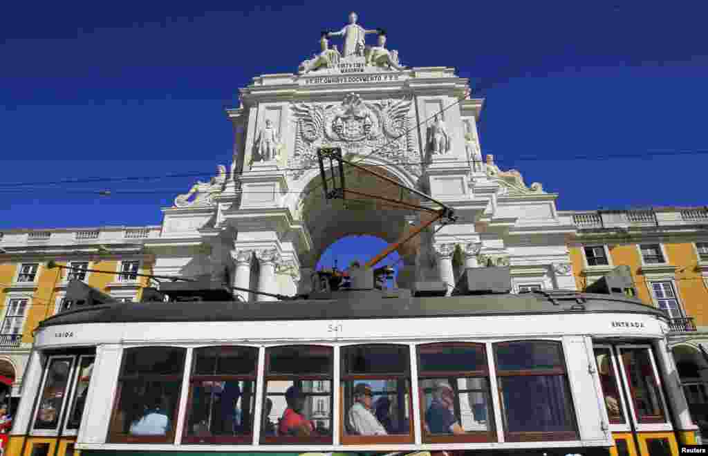 Para penumpang naik trem yang melewati lengkungan utama Praca do Comercio, yang merupakan kantor Departemen Keuangan Portugal di Lisabon.