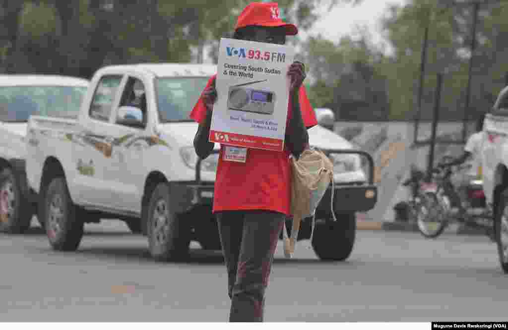 The launch of the 93.5 Voice of America station is... great news for all of us South Sudanese. We need our news and events to be going out to other people. - Chubarex from Juba A young woman braves the traffic in Juba, South Sudan, with a poster advertising the launch of Voice of America&#39;s new FM transmitter. The transmitter, which was ceremoniously launched on Thursday, March 21, 2013, joins a network that bring Voice of Americ