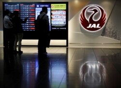 Pria berdiri di samping logo Japan Airlines (JAL), di tengah wabah COVID-19, di Bandara Internasional Tokyo, yang biasa disebut Bandara Haneda di Tokyo, Jepang, 30 Oktober 2020. (Foto: REUTERS/Issei Kato)