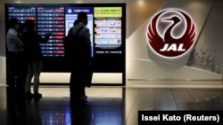 Pria berdiri di samping logo Japan Airlines (JAL), di tengah wabah COVID-19, di Bandara Internasional Tokyo, yang biasa disebut Bandara Haneda di Tokyo, Jepang, 30 Oktober 2020. (Foto: REUTERS/Issei Kato)