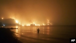 Seorang pria menyaksikan kebakaran hutan mendekati pantai Kochyli dekat desa Limni di pulau Evia, sekitar 160 kilometer utara Athena, Yunani, Jumat, 6 Agustus 2021. (AP Photo/Thodoris Nikolaou)