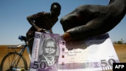 FILE - A South Sudanese refugee shows his country's 50-pound note as he heads across the border in Sudan's White Nile state on Feb. 28, 2017.