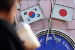 FILE - A woman walks past an advertisement featuring Japanese and South Korean flags at a shop in the Shin Okubo area in Tokyo, Aug. 2, 2019.