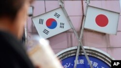 FILE - A woman walks past an advertisement featuring Japanese and South Korean flags at a shop in the Shin Okubo area in Tokyo, Japan, Aug. 2, 2019.