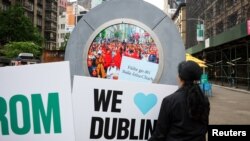 Personas sostienen carteles saludando a la gente durante la revelación de The Portal, una escultura de tecnología pública que conecta directamente entre Dublín, Irlanda y el distrito Flatiron en Manhattan, en la ciudad de Nueva York, el 8 de mayo de 2024.