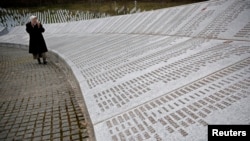 FILE - Fadila Efendic prays near memorial plaques at the Potocari genocide memorial center near Srebrenica, March 18, 2015. 