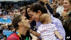 FILE - Michael Phelps celebrates winning a gold medal in the men's 200-meter butterfly with Nicole Johnson and baby Boomer during the swimming competitions at the 2016 Summer Olympics, in Rio de Janeiro, Brazil. 