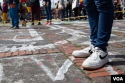 A protester stands on painted outlines of bodies representing the Colombians who disappeared during previous protests, in Bogota, July 20, 2021. (Megan Janetsky/VOA)