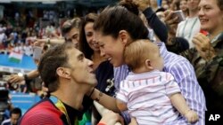 Michael Phelps merayakan kemenangannya meraih medali emas pada gaya kupu-kupu 200 meter pria bersama Nicole Johnson dan bayi mereka Boomer pada Olimpiade 2016 di Rio de Janeiro, Brazil. (Foto: Dok)