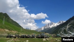 Indian army soldiers walk past their parked trucks at a makeshift transit camp before heading to Ladakh, near Baltal, southeast of Srinagar, June 16, 2020.