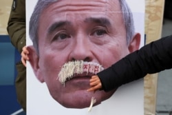 FILE - A protester plucks face mustache from a picture of U.S. Ambassador to South Korea Harry Harris during a rally to denounce the United States' policies near the U.S. embassy in Seoul, South Korea, Dec. 13, 2019.