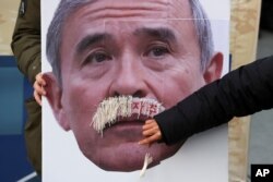 FILE - A protester plucks face mustache from a picture of U.S. Ambassador to South Korea Harry Harris during a rally to denounce the United States' policies near the U.S. embassy in Seoul, South Korea, Dec. 13, 2019.